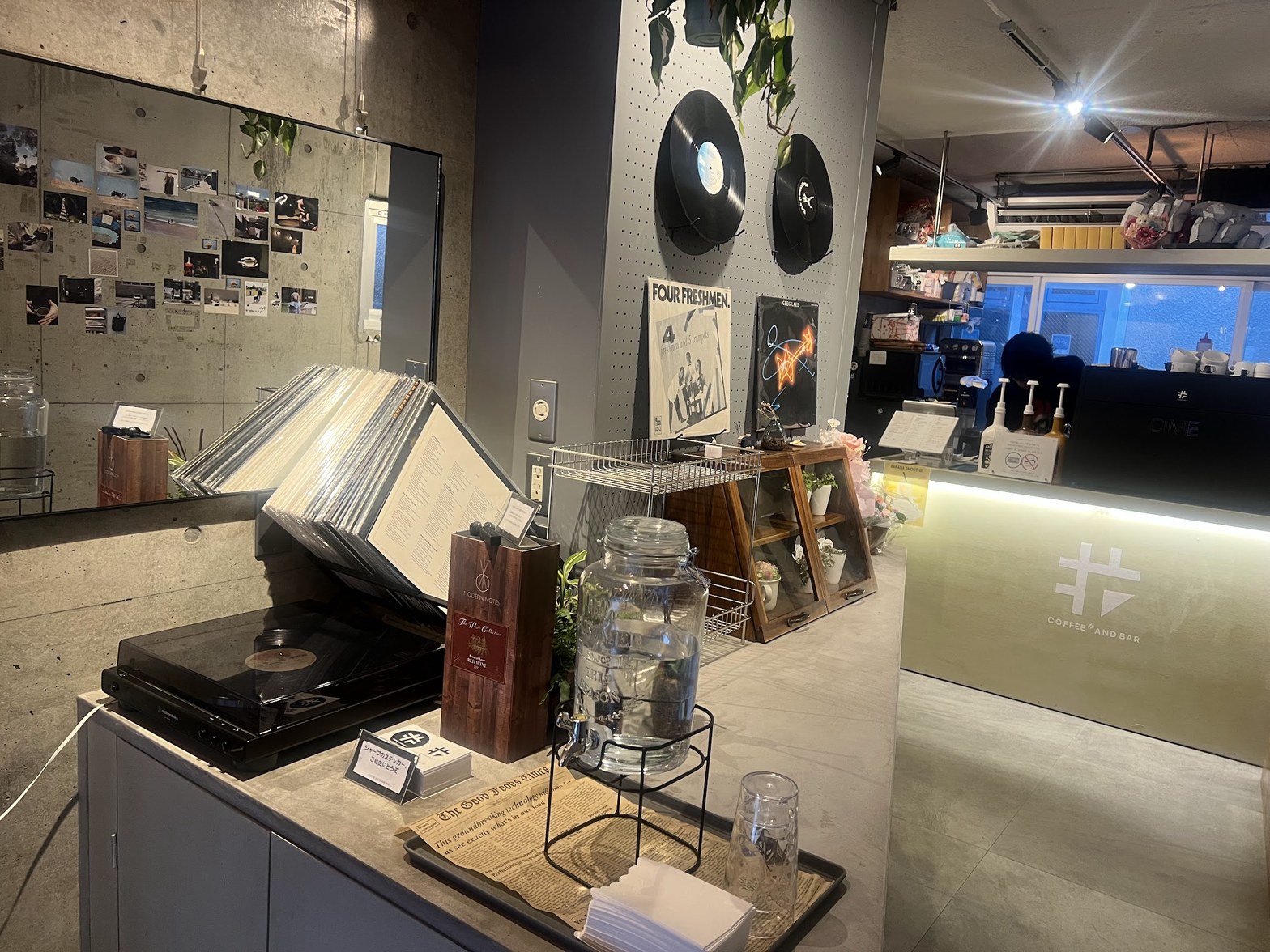 ターンテーブルの上に置かれたレコード、壁に飾られた複数のレコードジャケット、手前に積まれたレコード群とCOFFEE SHARP AND BARのロゴが入ったカウンター